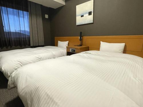 two beds in a hotel room with white sheets at Hotel Route-Inn Omaezaki in Omaezaki