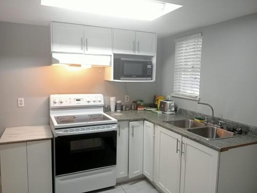 a kitchen with white cabinets and a stove and a sink at Small Cozy Private Room For 1 or 2 Travellers in a Great Location (King George Boulevard, Surrey) in Surrey