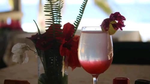 een vaas met bloemen en een glas wijn bij White Beach Bungalow & Restaurant in Lénakel