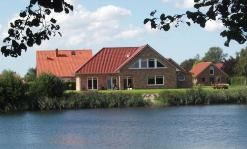 een huis met een rood dak naast een waterlichaam bij Haus am Kiessee - Landromantik mit traumhaftem Seeblick in Nenndorf