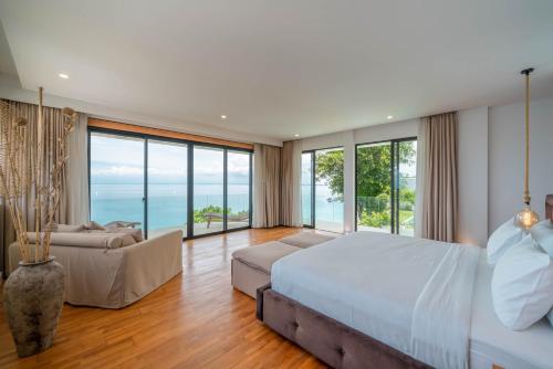 a bedroom with a bed and a couch and windows at Villa Namaskar - Iconic 5BR Cliff Top Villa - 180° Ocean View in Jimbaran