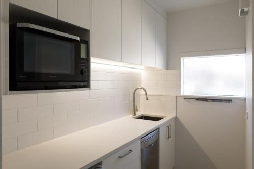 a white kitchen with a sink and a microwave at Stay Coastal - Apartments in Auckland