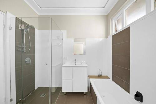 La salle de bains blanche est pourvue d'un lavabo et d'une douche. dans l'établissement River View Oasis: Spacious 3-Bed House with Pool, à Sydney