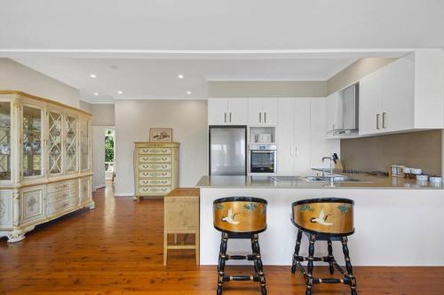 a kitchen with white cabinets and two bar stools at River View Oasis: Spacious 3-Bed House with Pool in Sydney