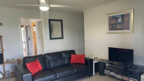 a living room with a black leather couch and a tv at Lowset home with attached Granny Flat - Doomba Dr, Bongaree in Bongaree