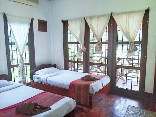 a bedroom with two beds and large windows at VangVieng Ruby'Homestay in Vang Vieng
