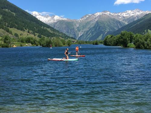 two people on paddle boards on a lake with mountains at Nanisgarten - Grannys flat in Obergesteln