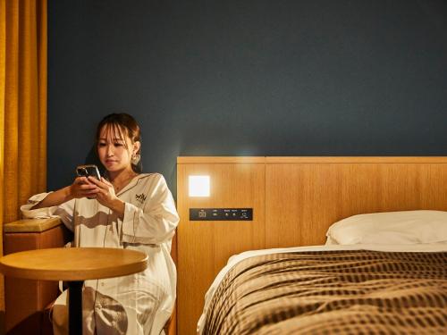 Kansai Airport Washington Hotel في إيزوميسانو: امرأة جالسة بجانب السرير تبحث في جوالها