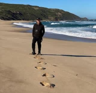 a man standing on a beach with footprints in the sand at Sky Ship 1 - Luxury Off-Grid Eco Accommodation in Cape Otway