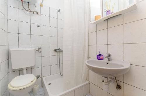 a white bathroom with a toilet and a sink at Apartments Laguna in Stomorska