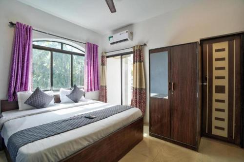 1 dormitorio con 1 cama grande y cortinas moradas en Baga Treasures, en Goa