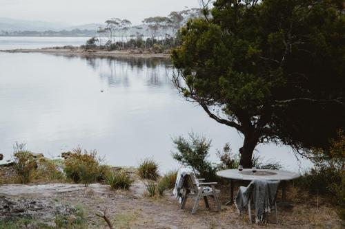 a table and chairs sitting next to a lake at Sunken Sea Shack - waterfront getaway in Eggs and Bacon Bay
