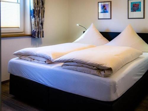 uma cama com lençóis brancos e almofadas em Cosy apartment in Bolsterlang em Bolsterlang