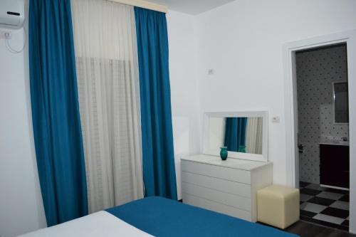 a bedroom with blue curtains and a bed and a mirror at Villa August Ksamil in Ksamil