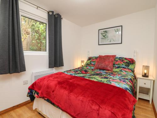a bedroom with a bed with a red comforter and a window at Palm Lodge in Penzance