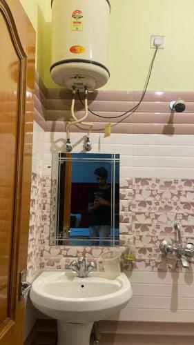 La salle de bains est pourvue d'un lavabo et d'une personne prenant une photo dans un miroir. dans l'établissement Ganga Vardan hotel, à Rishikesh