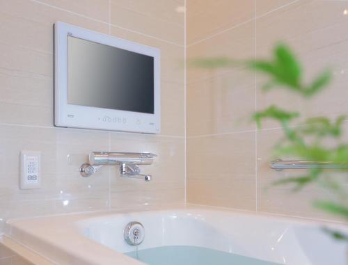 a television on a wall above a bath tub at Odakyu Hotel Century Sagami Ono in Sagamihara