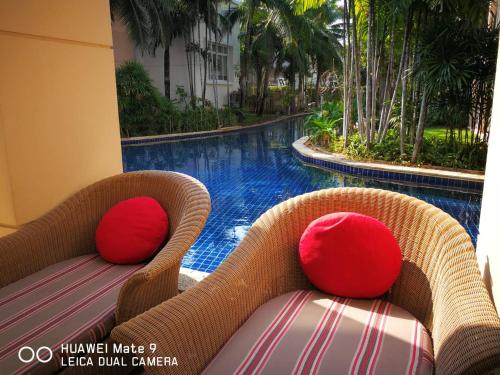 a wicker chair with red pillows next to a swimming pool at Hua Hin Blue Lagoon in Cha Am