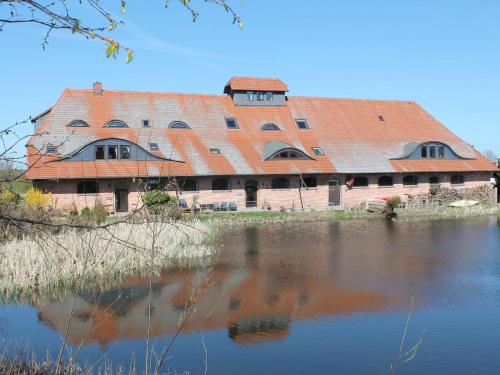 an old building with an orange roof next to a body of water at Rustic style Apartment in Buschenhagen with Garden in Buschenhagen