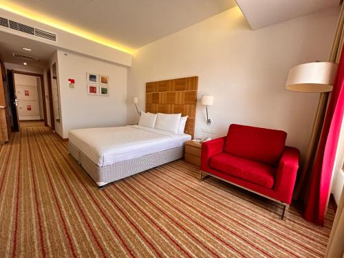 a hotel room with a bed and a red chair at Golden Tulip Muscat in Muscat