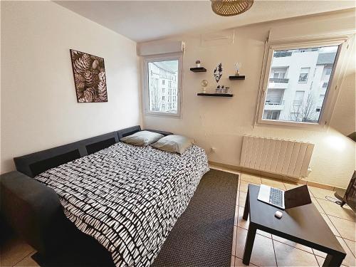 a bedroom with a bed and a table and two windows at Cosy appartement - Parking Privé Gratuit in Chambéry