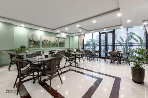 un restaurante con mesas, sillas y ventanas en Nature Hanoi Hotel en Hanói