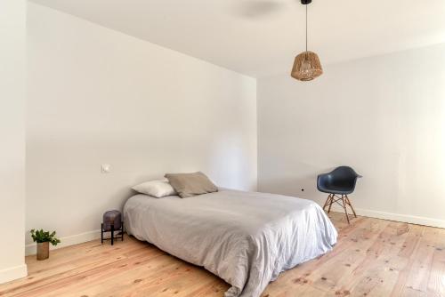 a white bedroom with a bed and a chair at le maquens - parking gratuit - wifi - netflix in Carcassonne