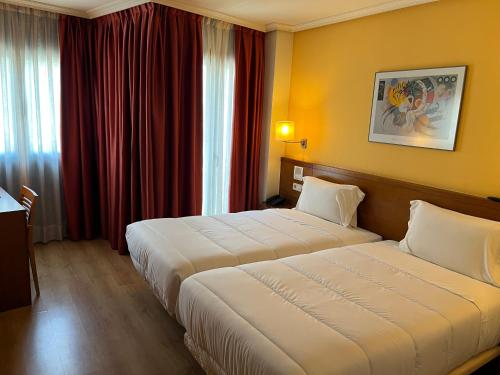 two beds in a hotel room with red curtains at U Hotel Ogalia Vigo in Vigo