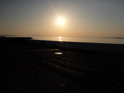 a sunset on the beach with the sun setting over the water at EZ HOTEL Kansai Airport Seaside in Izumi-Sano