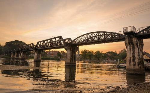 a train bridge over a river with the sun setting at Noot's Guesthouse in Kanchanaburi