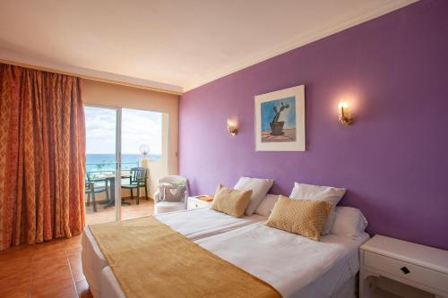 1 dormitorio con pared morada, cama y mesa en BJ Playa Blanca en Sa Coma