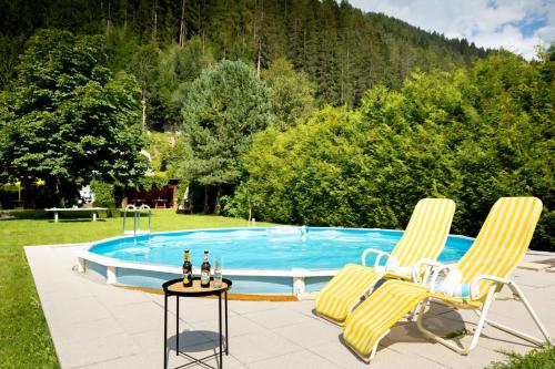 uma piscina com duas cadeiras e uma mesa com bebidas em Der Thomataler Wirt em Thomatal
