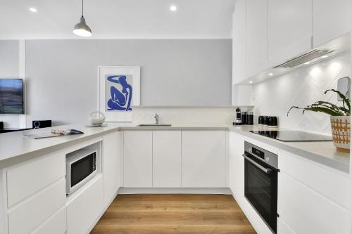 a white kitchen with white cabinets and a black dishwasher at Stylish, Sunny & Spacious 2 Bedroom Apartment, Mosman in Sydney