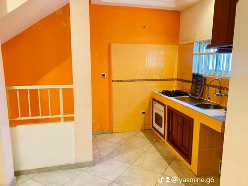 uma cozinha com paredes cor de laranja, um lavatório e um fogão em Yasmine Immo em Cotonou