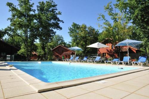 a large swimming pool with chairs and umbrellas at Tidy chalet in the woods of the beautiful Dordogne in Souillac