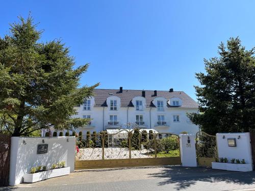 a white building with a gate and trees at Pensjonat Zenit in Ustronie Morskie