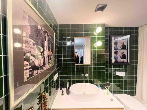 uma casa de banho com azulejos verdes, um lavatório e um espelho. em New appartment with art collection em Vilnius