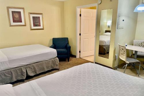 a hotel room with two beds and a chair and a mirror at Suburban Studios Fort Myers Cape Coral in Fort Myers