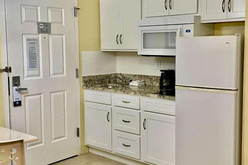 a kitchen with white cabinets and a white refrigerator at Suburban Studios Fort Myers Cape Coral in Fort Myers