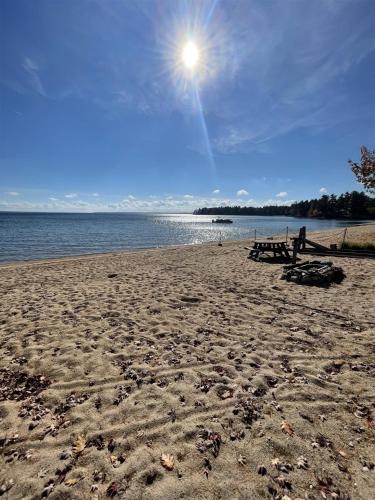 a sandy beach with the sun shining over the water at 1901 HOUSE LIMIT 10 cottage in North Sebago