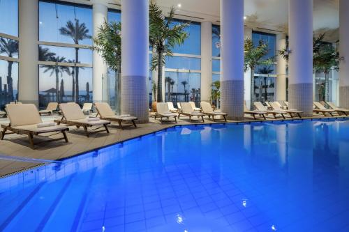 a hotel pool with chairs and palm trees at Vert Dead Sea by AFI Hotels in Ein Bokek