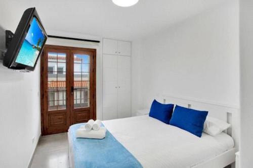 a white bed with blue pillows and a flat screen tv at Beautiful Apartment El Unicornio De Paula in Candelaria