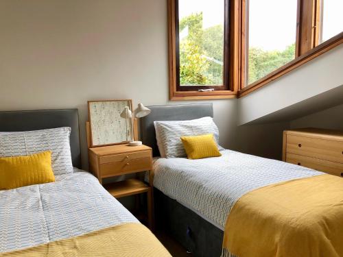 two beds in a room with two windows at A Unique, Rural, Modern Annexe with Large Garden, Games, Tennis Court & EV Point in Chichester
