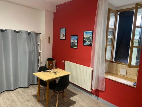 Cette chambre comprend une table et un mur rouge. dans l'établissement L'unico, à Bagnères-de-Bigorre