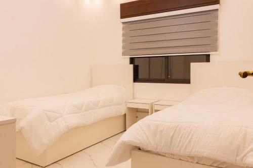 a white bedroom with two beds and a window at Prestige hotel apartment in Amman