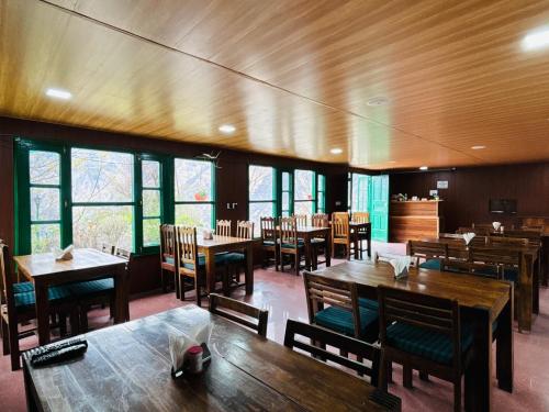 een restaurant met houten tafels, stoelen en ramen bij Himalayan High, Auli, By Himalayan Eco Lodges in Joshimath