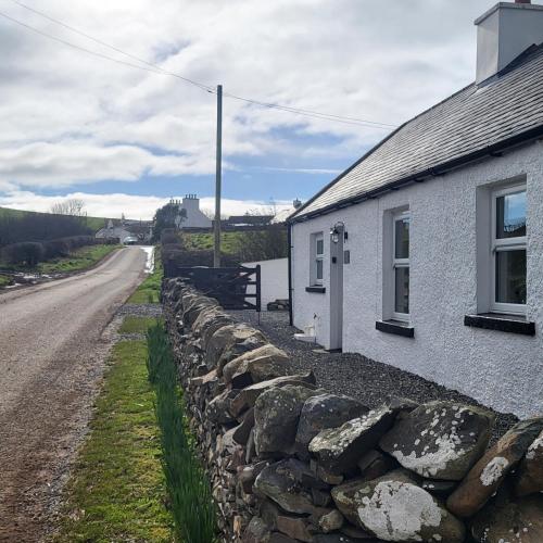 a stone wall next to a building next to a road at RAWSON COTTAGE LOVELY 2 BEDROOM SEMI RURAL in Stranraer