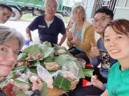 a group of people sitting around a table with food at Wooden floor house Ngọc trinh Homestay in Bản Qua