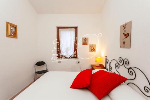 a white bedroom with a red pillow on a bed at Domus Dejana in San Teodoro