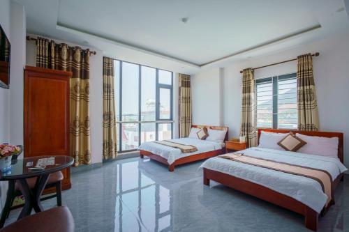 a bedroom with two beds and a table and windows at Phú Xuân Hotel in Quy Nhon